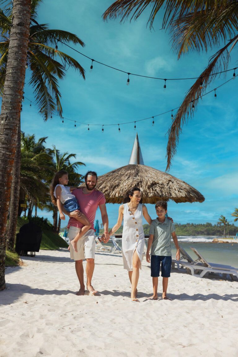 Familia caminando de la mano por la arena bajo las palmeras de Playa Escondida