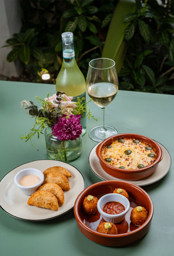 Mesa para compartir con panzerotti, croquetas, flores y una copa de vino blanco