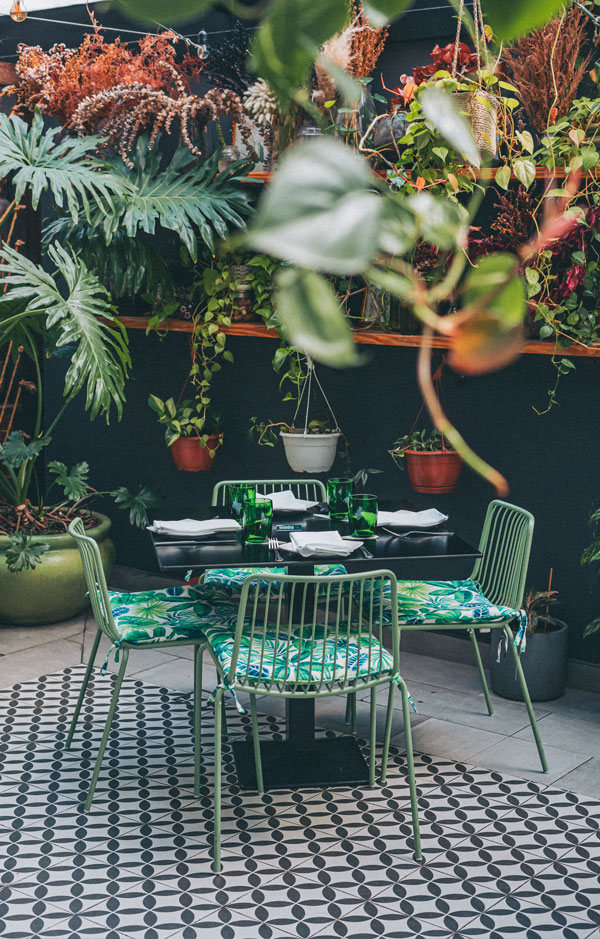 Mesas y sillas verdes rodeadas de plantas en la terraza de Botanica Pizza