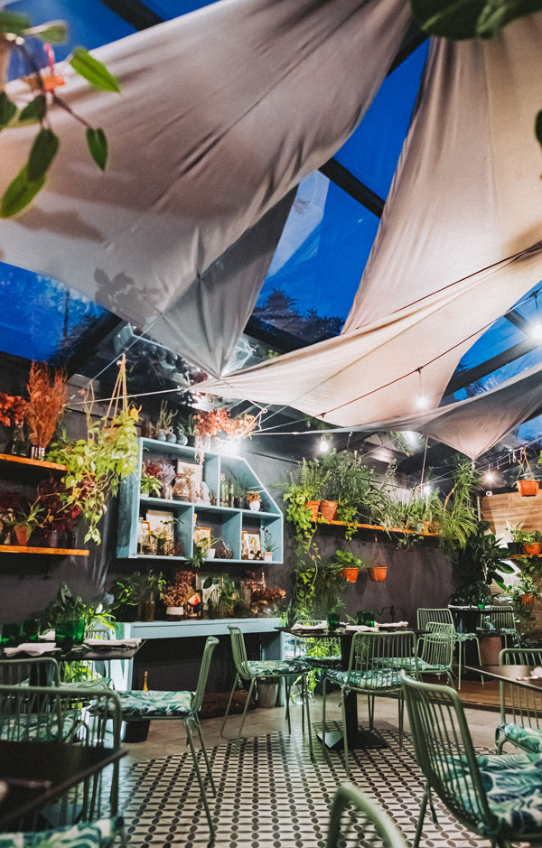 Terraza de Botanica Pizza con toldos, plantas colgantes y piso de baldosas