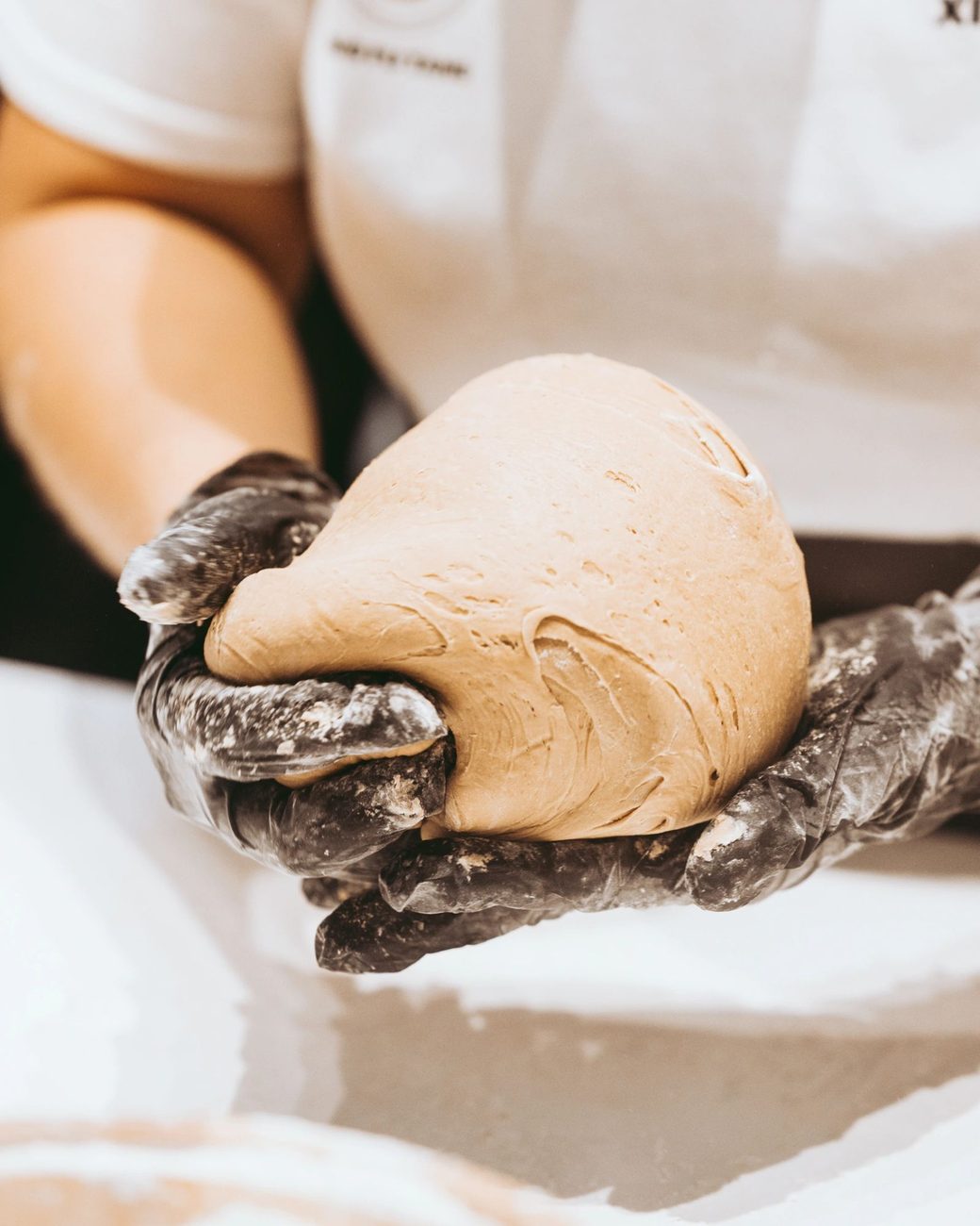Manos con guantes sosteniendo la masa de tapioca recién amasada para hacer las perlas de Xing Fu Tang