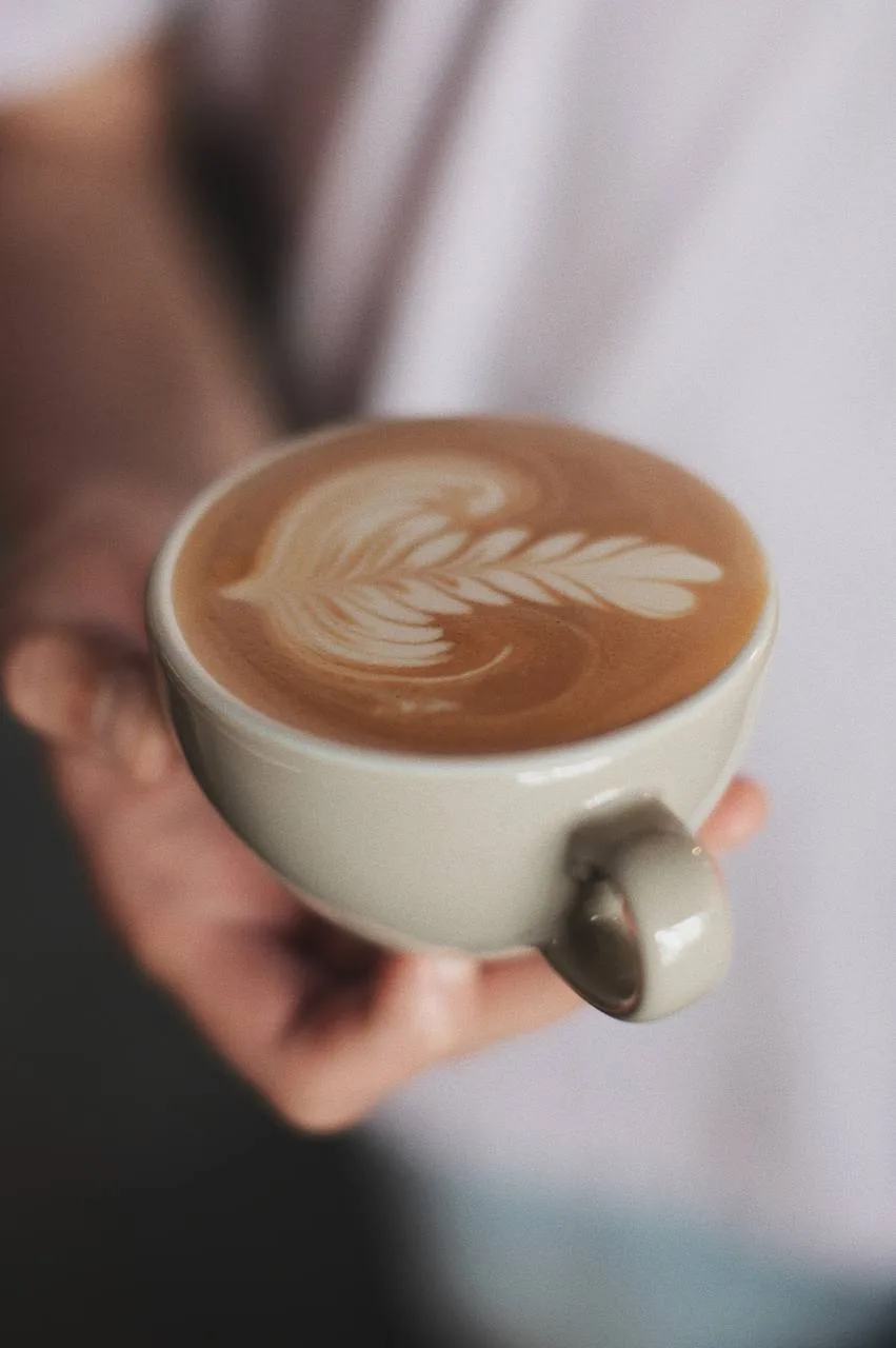 Cappuccino con arte latte en taza blanca sostenida con ambas manos