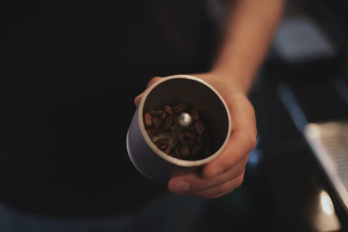 Mano sosteniendo un molino manual lleno de granos de café tostado