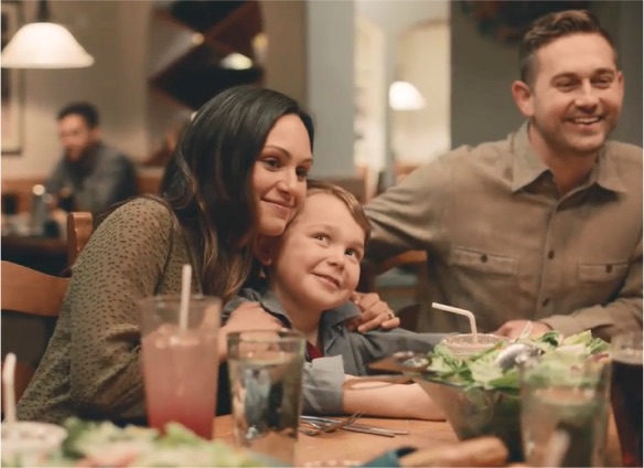 Familia sonriendo alrededor de una mesa de Olive Garden con ensalada y bebidas