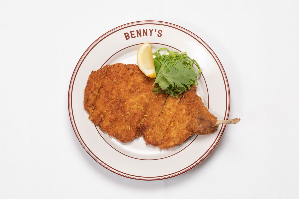Milanesa de cerdo empanizada con limón y hojas verdes en un plato de Benny's