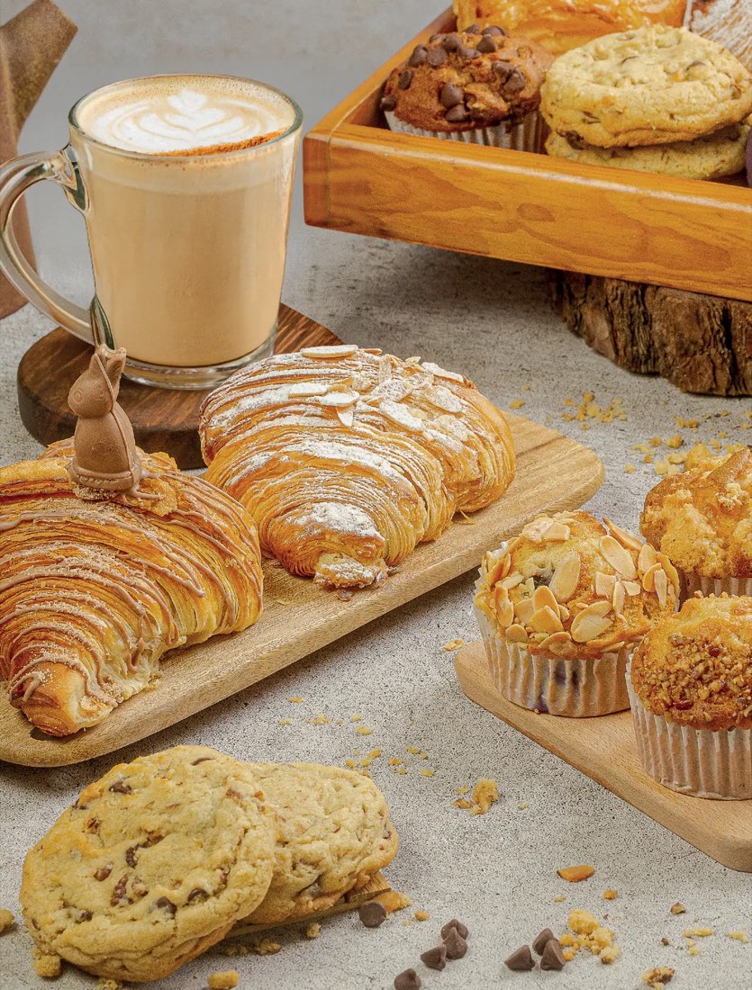 Latte con arte en la espuma junto a cornetti de almendras, muffins y galletas de la panadería de Tagers