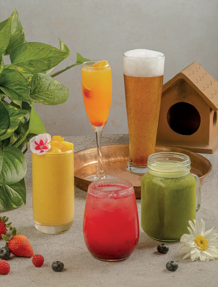 Smoothie de mango, mimosa, cerveza, agua fresca roja y jugo verde de Tagers sobre una mesa con flores