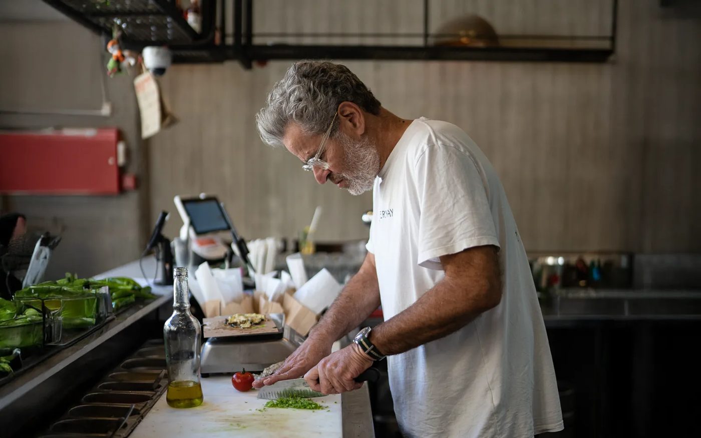 Cocinero picando hierbas frescas en la barra de Miznon junto a tomates y aceite de oliva