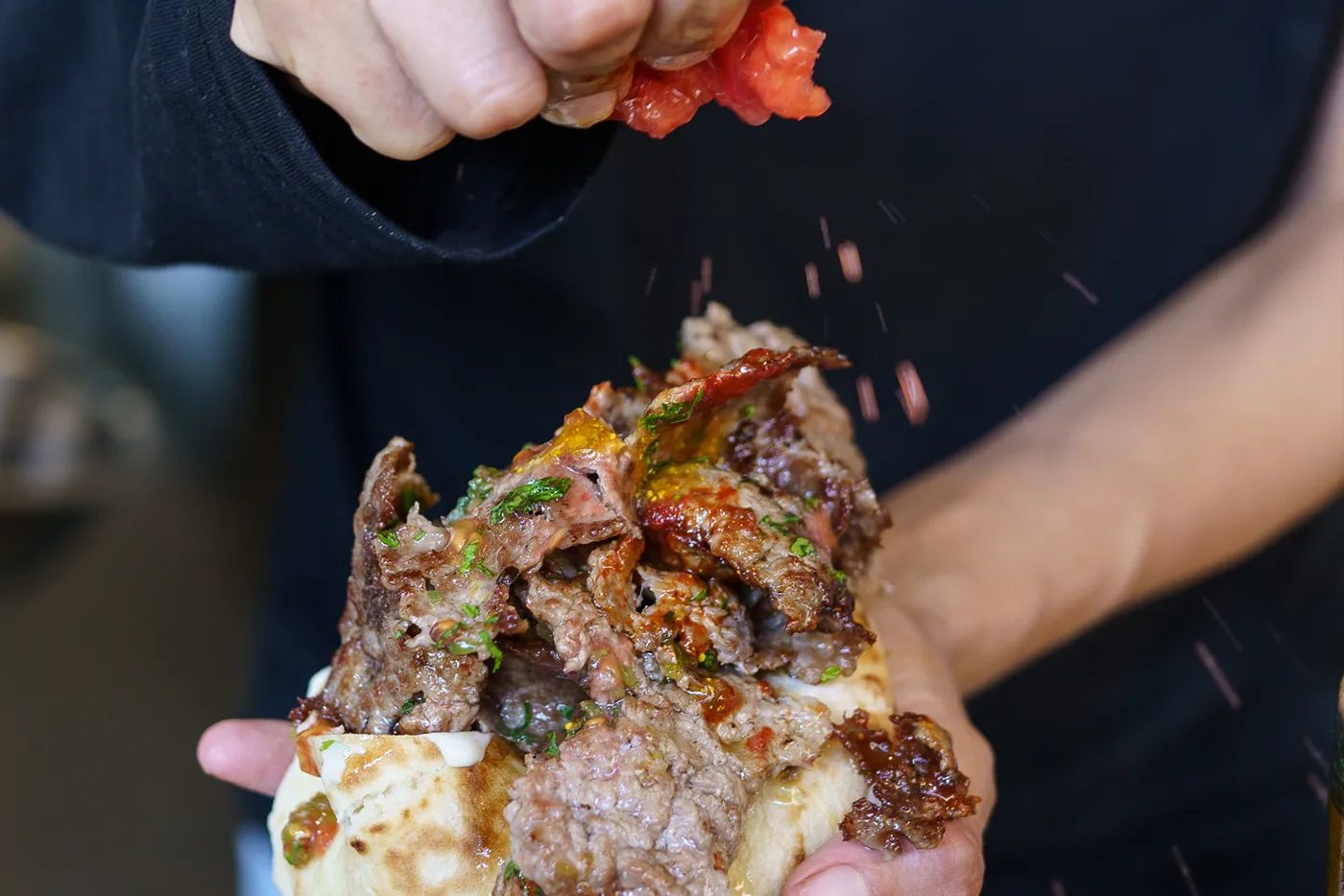 Manos exprimiendo tomate fresco sobre una pita abierta llena de carne y especias