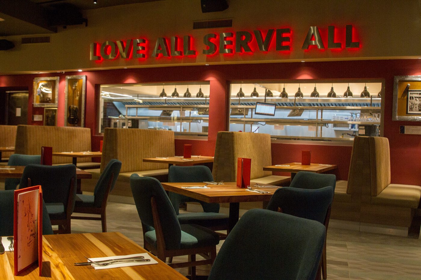 Salón principal de Hard Rock Cafe Caracas con el letrero Love All Serve All iluminado en rojo, guitarras enmarcadas y la cocina abierta